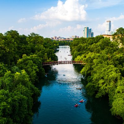 Aerial drone views of the green summer paradise down Barton Creek leading into Downtown Austin Texas with swimmers and kayakers and boats and canoes and Stand Up Paddle Boards enjoying the water