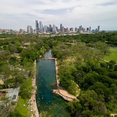 An aerial view of Barton Springs Pool in Zilker Metropolitan Park on a sunny day with Austin skyline in the background in Texas, USA
